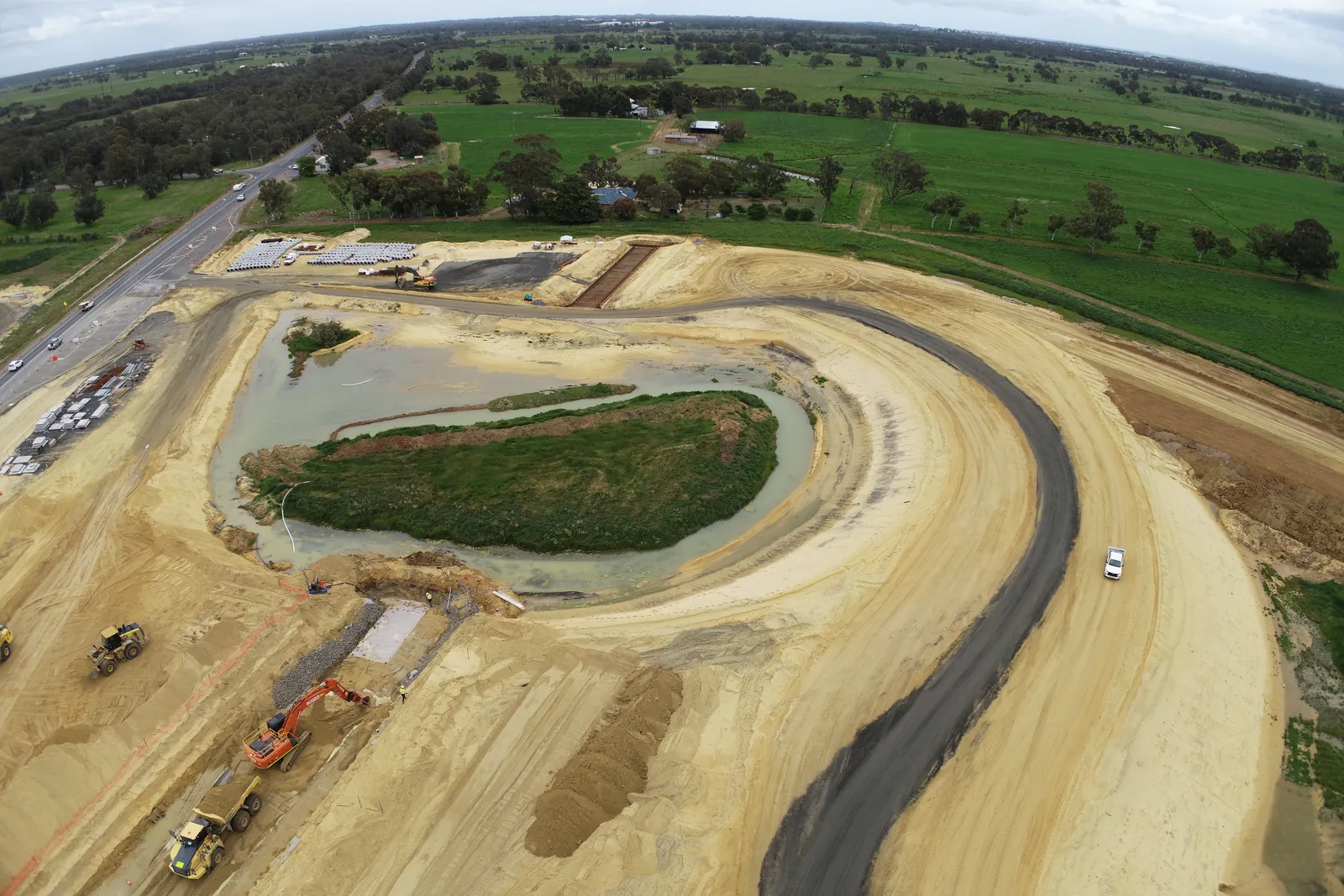 Drone view of a road ramp being built around a drainage basin, with machines on the formation